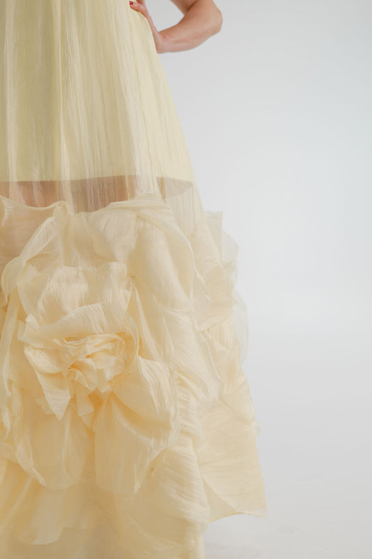 Close-up of the Aje Ecliptica pastel yellow gown showing the sheer textured fabric and sculptural rosette detailing at the hem.