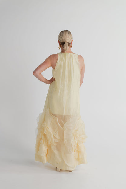 Back view of the Aje Ecliptica pastel yellow sleeveless gown showing its fluid shift silhouette and sculptural rosette hem.