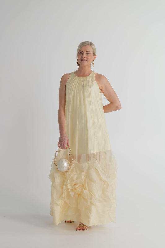 Aje Ecliptica pastel yellow gown with fluid swing silhouette and sculptural rosette hem, styled with the Verano Hill Ondine pearl pearlescent bag.