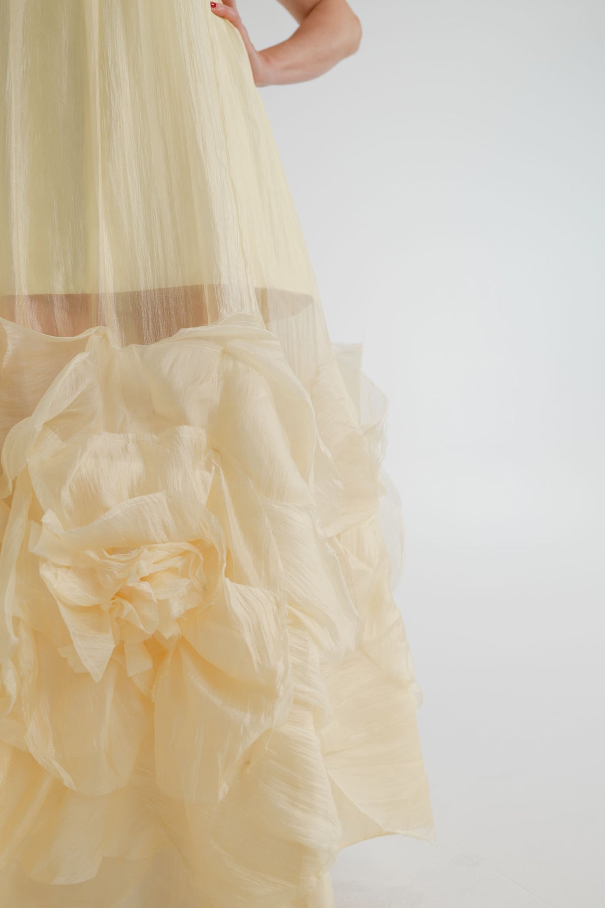 Close-up of the Aje Ecliptica pastel yellow gown showing the sheer textured fabric and sculptural rosette detailing at the hem.