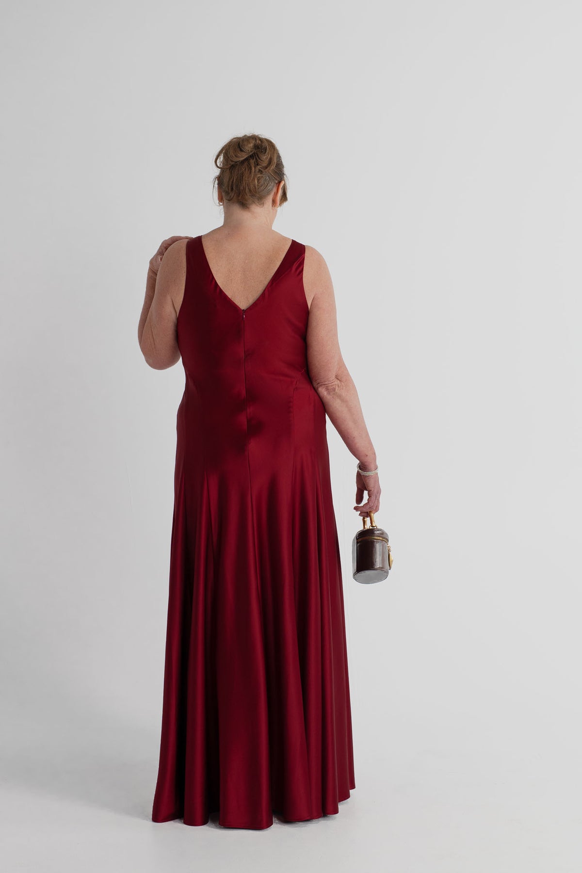 Back view of the Anna Quan Gabrielle wine satin gown showing the V-shaped back and fluid skirt, styled with the JW Pei Natalie dark brown bag.