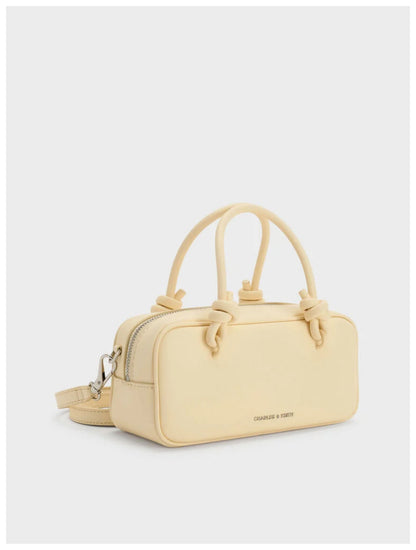 Charles & Keith Sammie pale butter yellow boxy bag with knotted handles and detachable shoulder strap, angled side view. 
