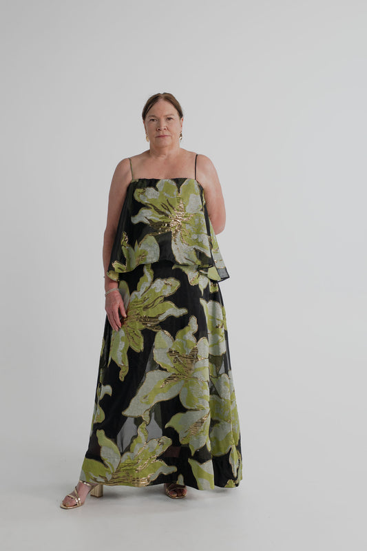Elliatt Elysia Tiered Gown in black with oversized green, silver and gold metallic floral detailing, thin straps and a layered tiered silhouette, shown full length from the front.
