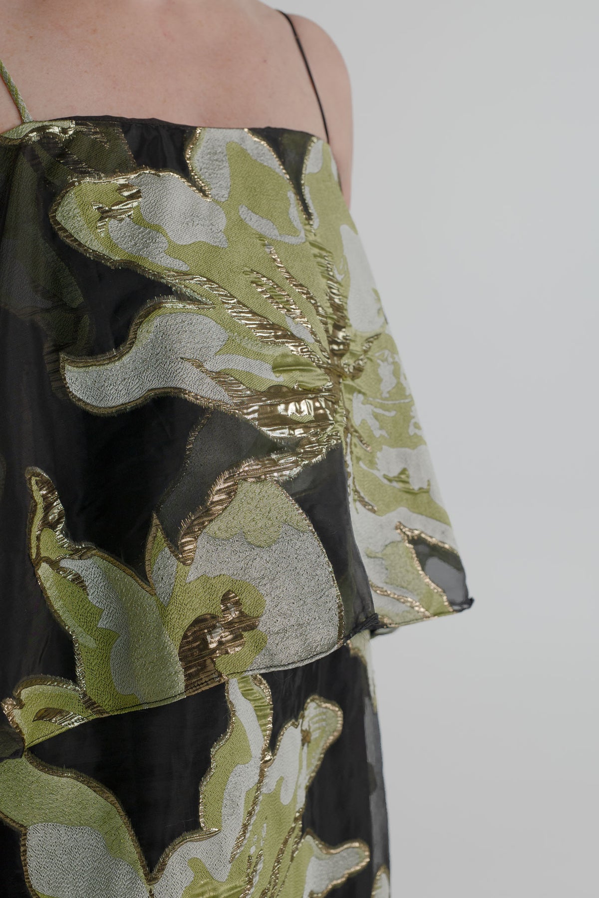Close-up of the Elliatt Elysia Tiered Gown highlighting the sheer black fabric and textured metallic green, silver and gold floral detailing.
