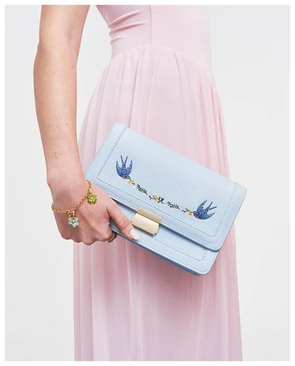 Model holding Fable England pale blue Blue Bird embroidered foldover bag as a clutch. 
