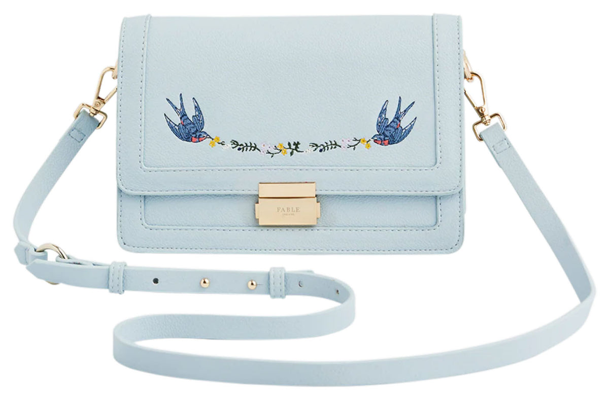 Fable England pale blue Blue Bird embroidered foldover bag with gold-tone clasp and detachable shoulder strap, front view. 
