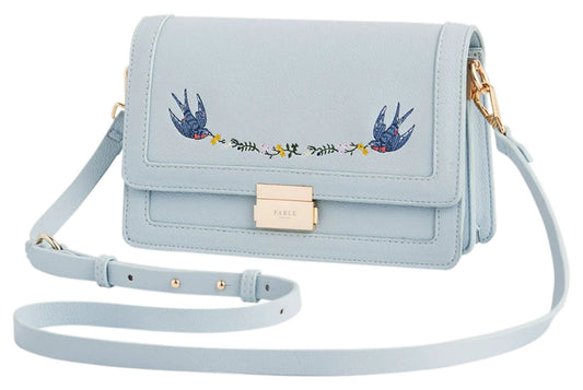 Angled view of Fable England pale blue Blue Bird embroidered foldover bag showing the structured side profile and shoulder strap. 
