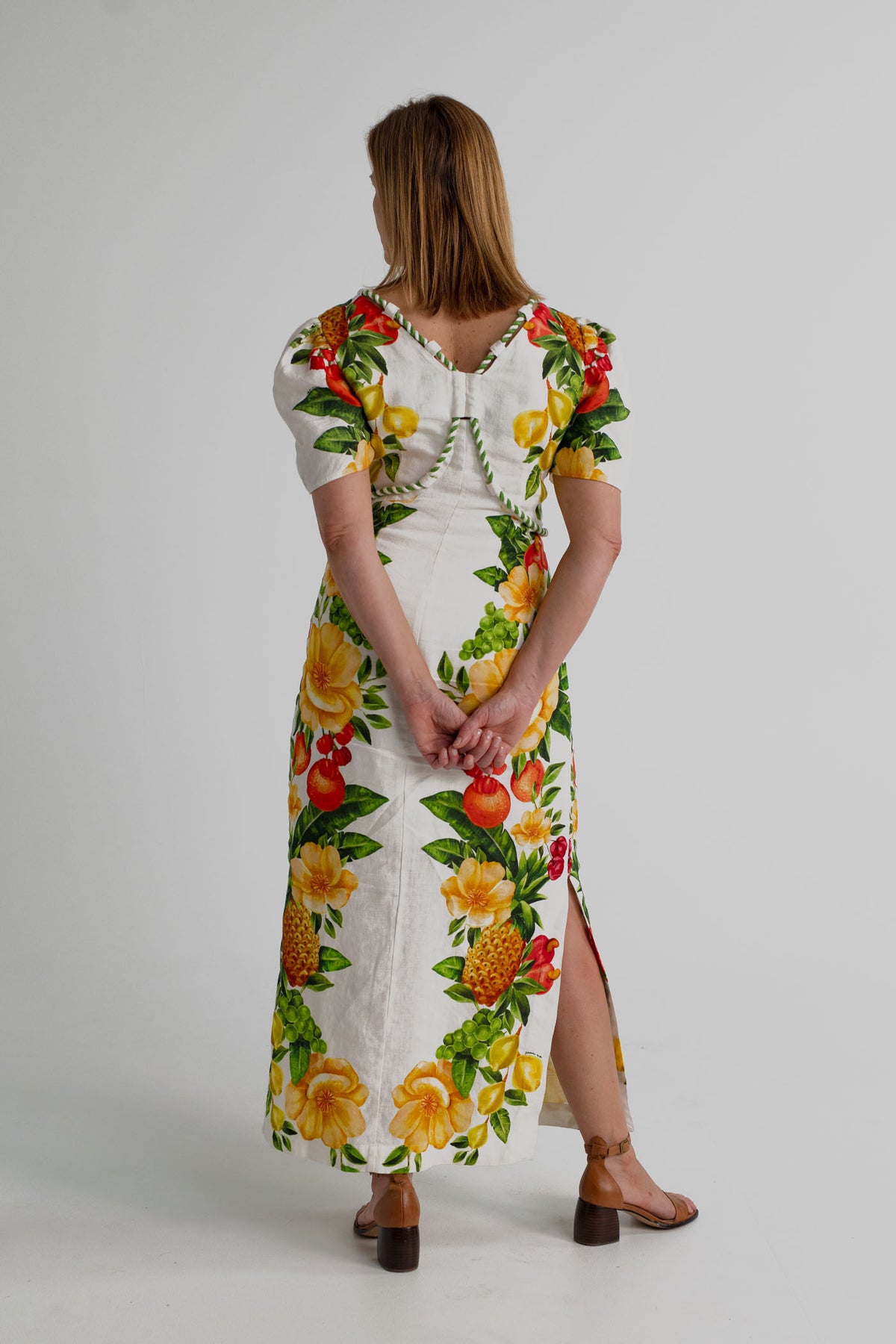 Back view of the Farm Rio Picnic Flowers Off-White Maxi showing the V-back, decorative piping and tropical fruit-and-floral print.
