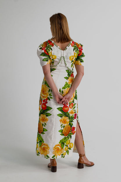 Back view of the Farm Rio Picnic Flowers Off-White Maxi showing the V-back, decorative piping and tropical fruit-and-floral print.
