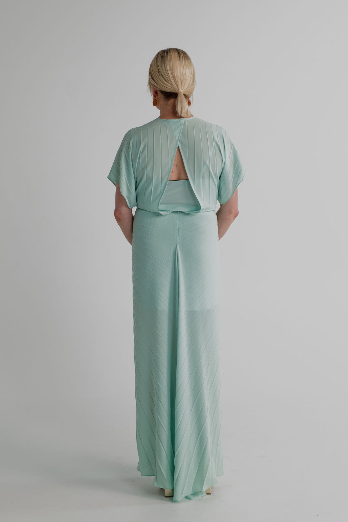Back view of the Georgia Hardinge Illusion mint pleated kaftan showing the open-back detail, flowing sleeves and full-length pleated silhouette.
