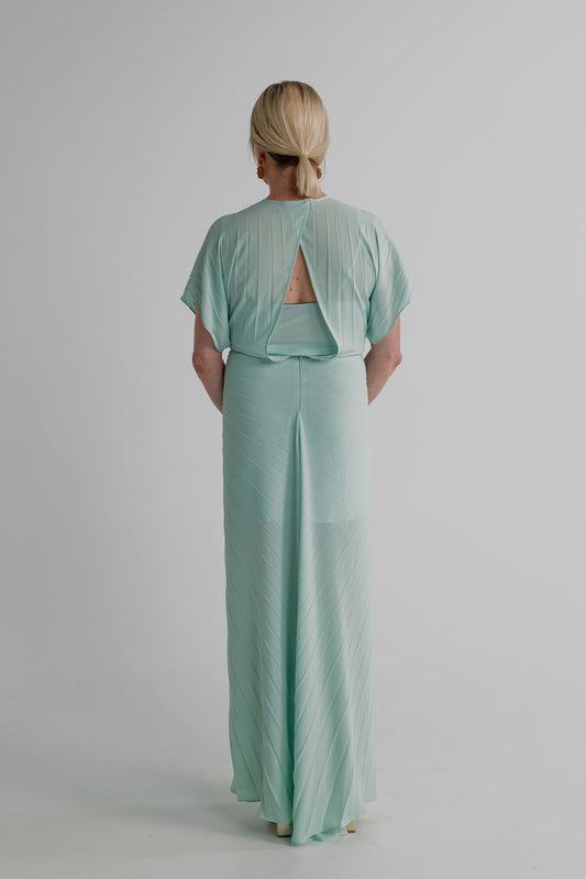 Back view of the Georgia Hardinge Illusion mint pleated kaftan showing the open-back detail, flowing sleeves and full-length pleated silhouette.
