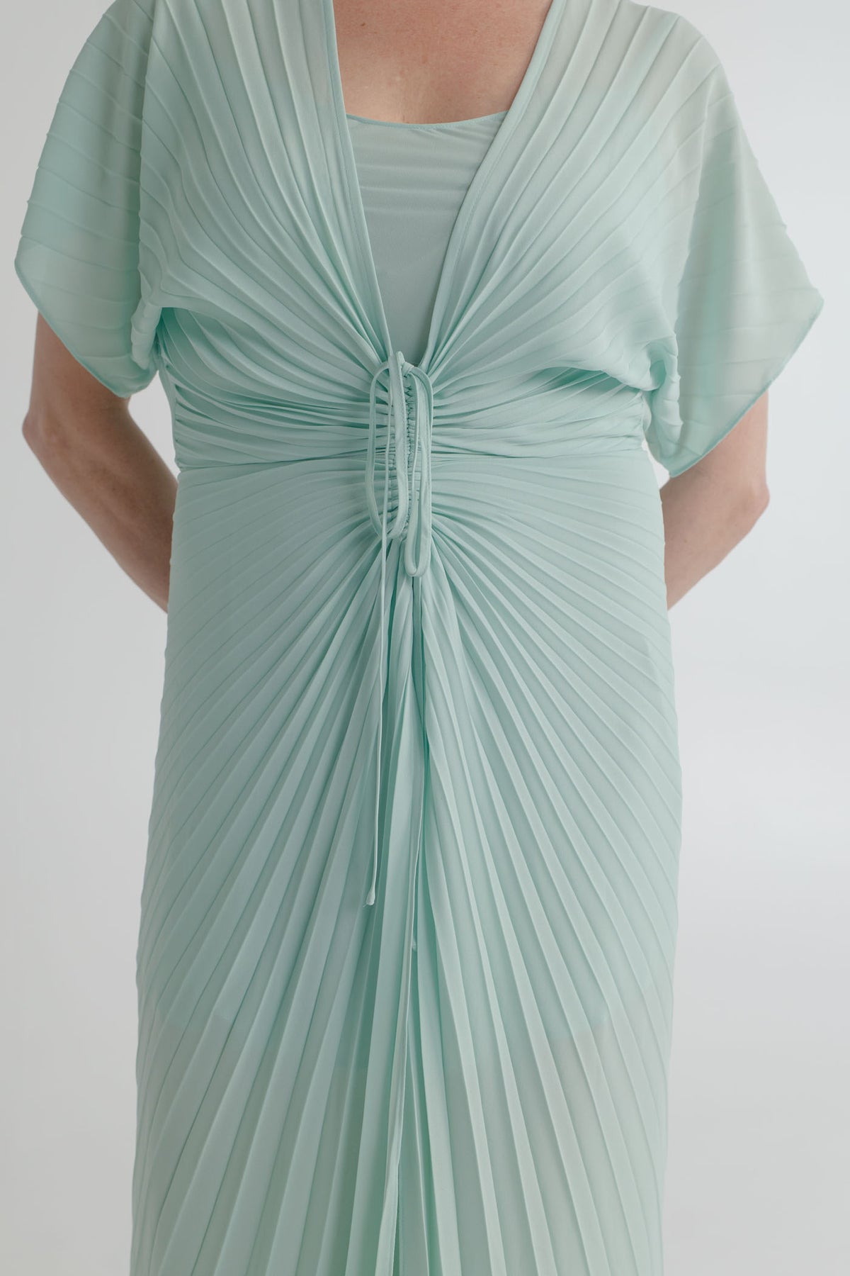 Close-up of the Georgia Hardinge Illusion mint kaftan showing the signature sunray pleating, gathered waist channel and tie detail.
