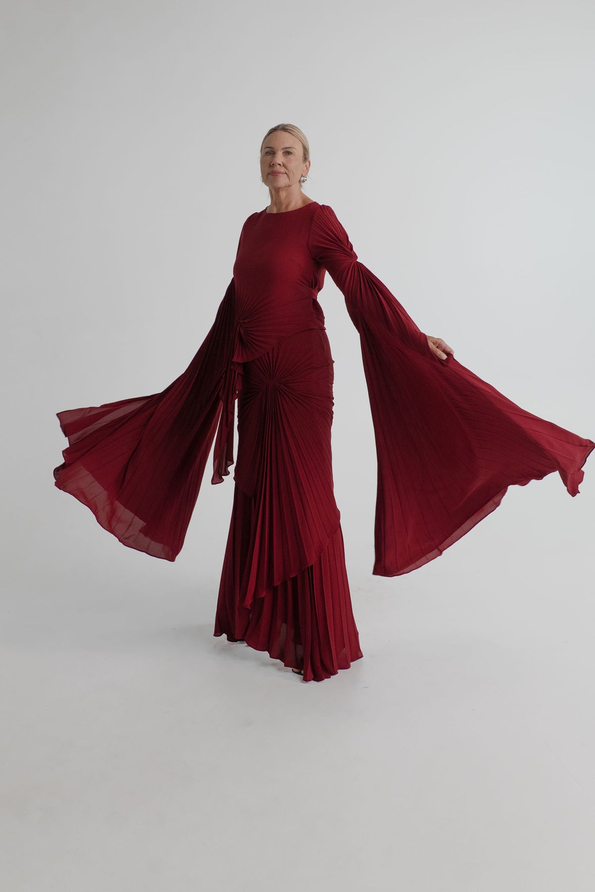 Georgia Hardinge Waterfall merlot gown in motion with sweeping pleated sleeves and cascading floor-length skirt.
