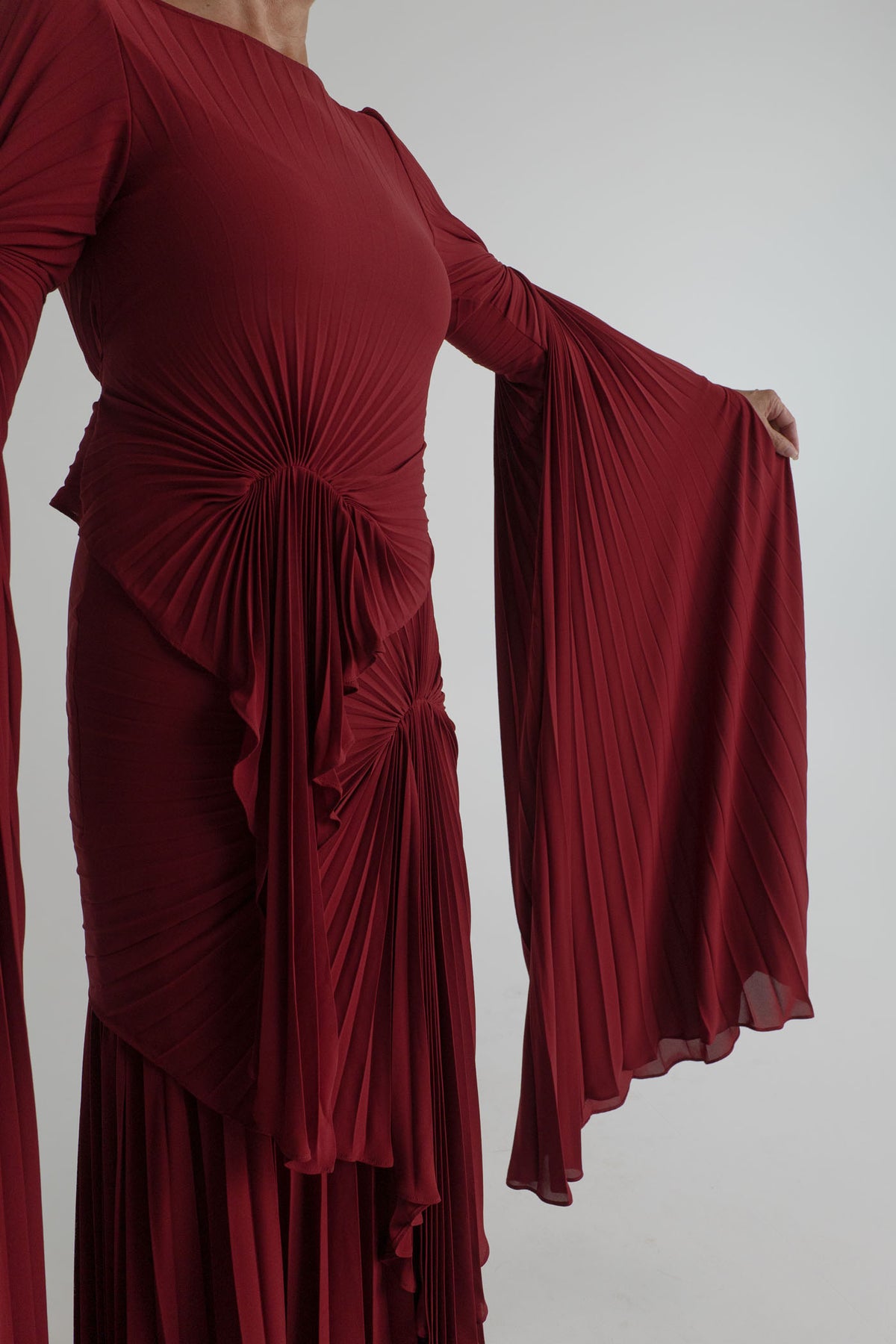 Detail of the Georgia Hardinge Waterfall merlot gown showing radiating pleats and the dramatic flowing sleeve panel.
