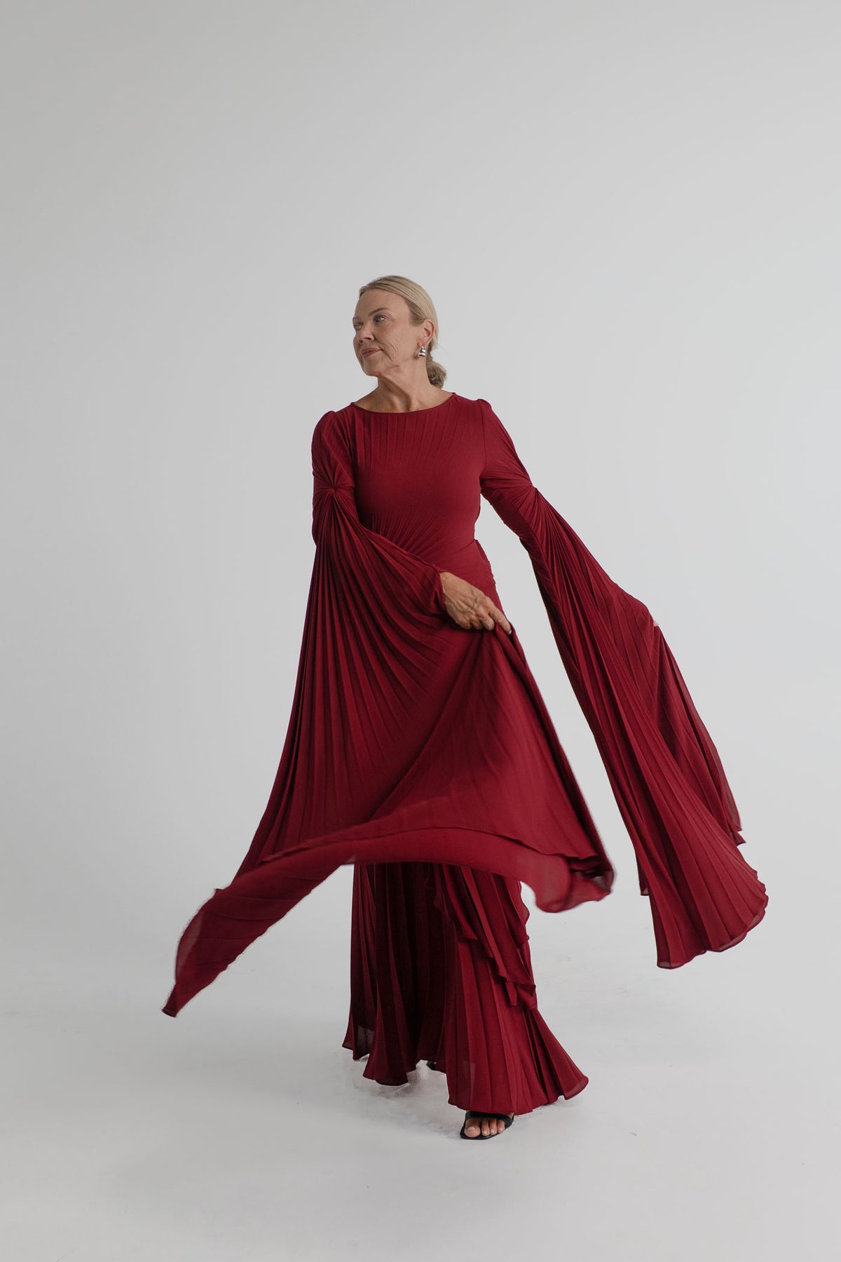 Georgia Hardinge Waterfall merlot pleated gown with cascading front panels and dramatic sleeves captured in motion.
