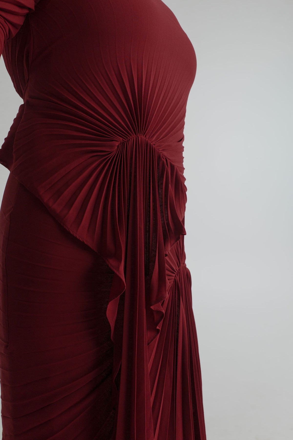 Close-up of the Georgia Hardinge Waterfall merlot gown showing sculptural sunray pleating and cascading waterfall detail at the waist.
