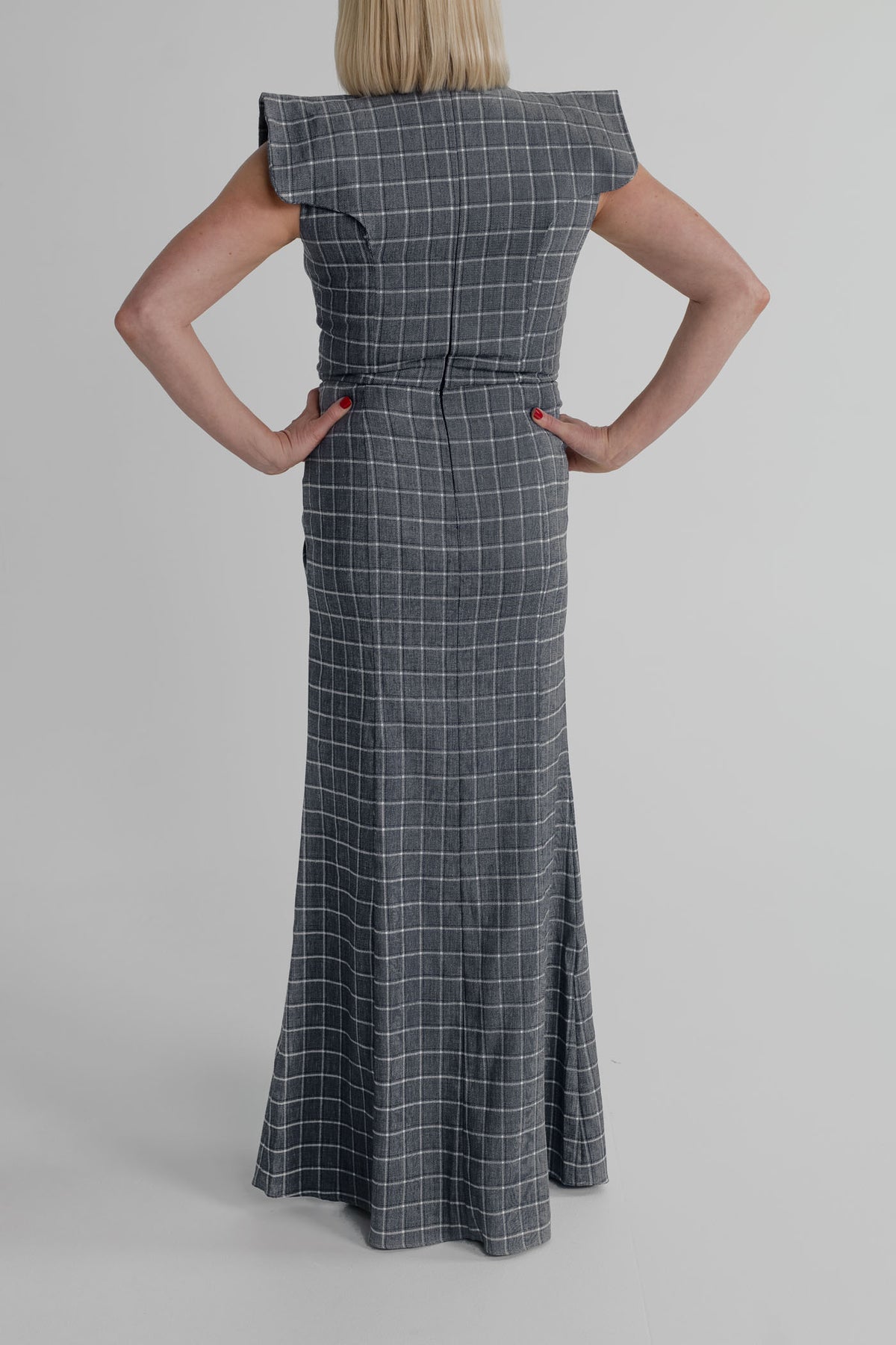 Back view of the IQ Collection Antonia Plaid Maxi showing the structured shoulders, fitted waist and long flared plaid skirt.
