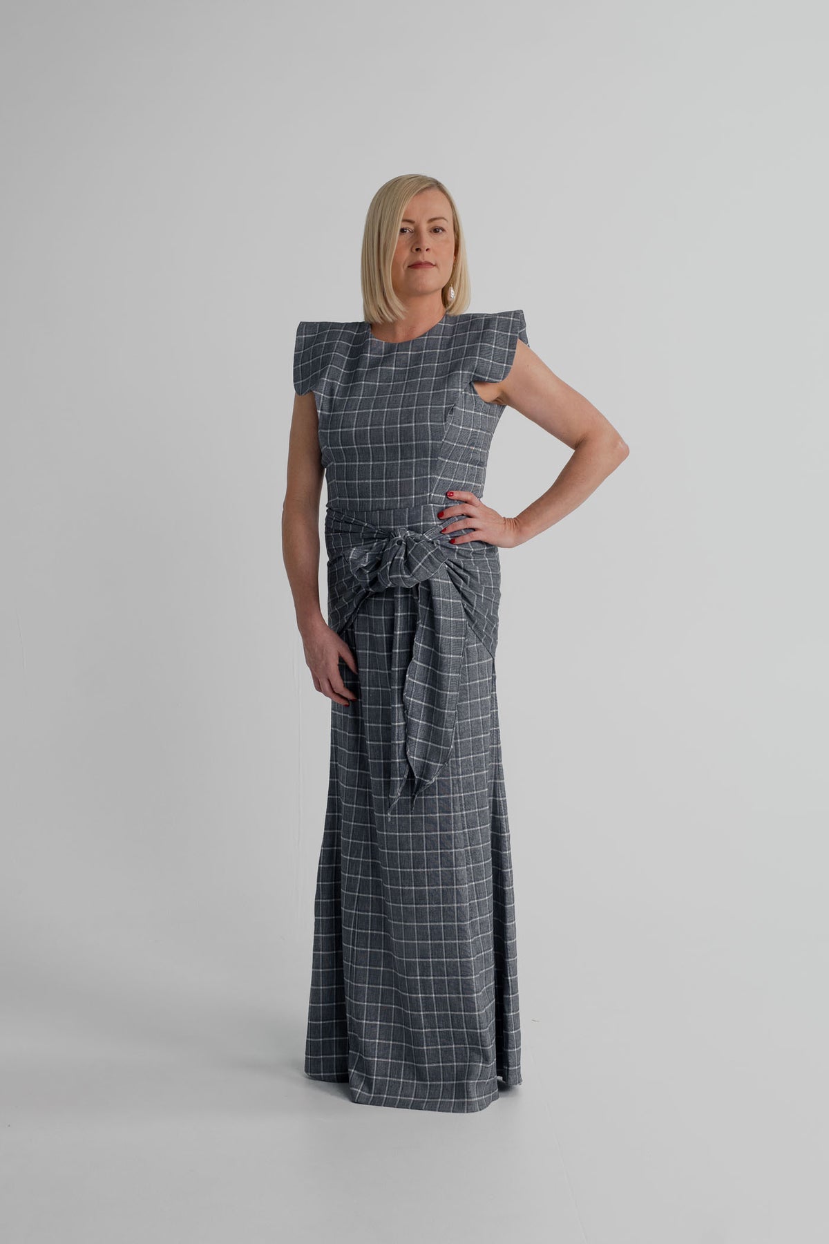 IQ Collection Antonia Plaid Maxi in charcoal grey check, featuring structured shoulders, a fitted bodice, statement waist tie and full-length skirt.
