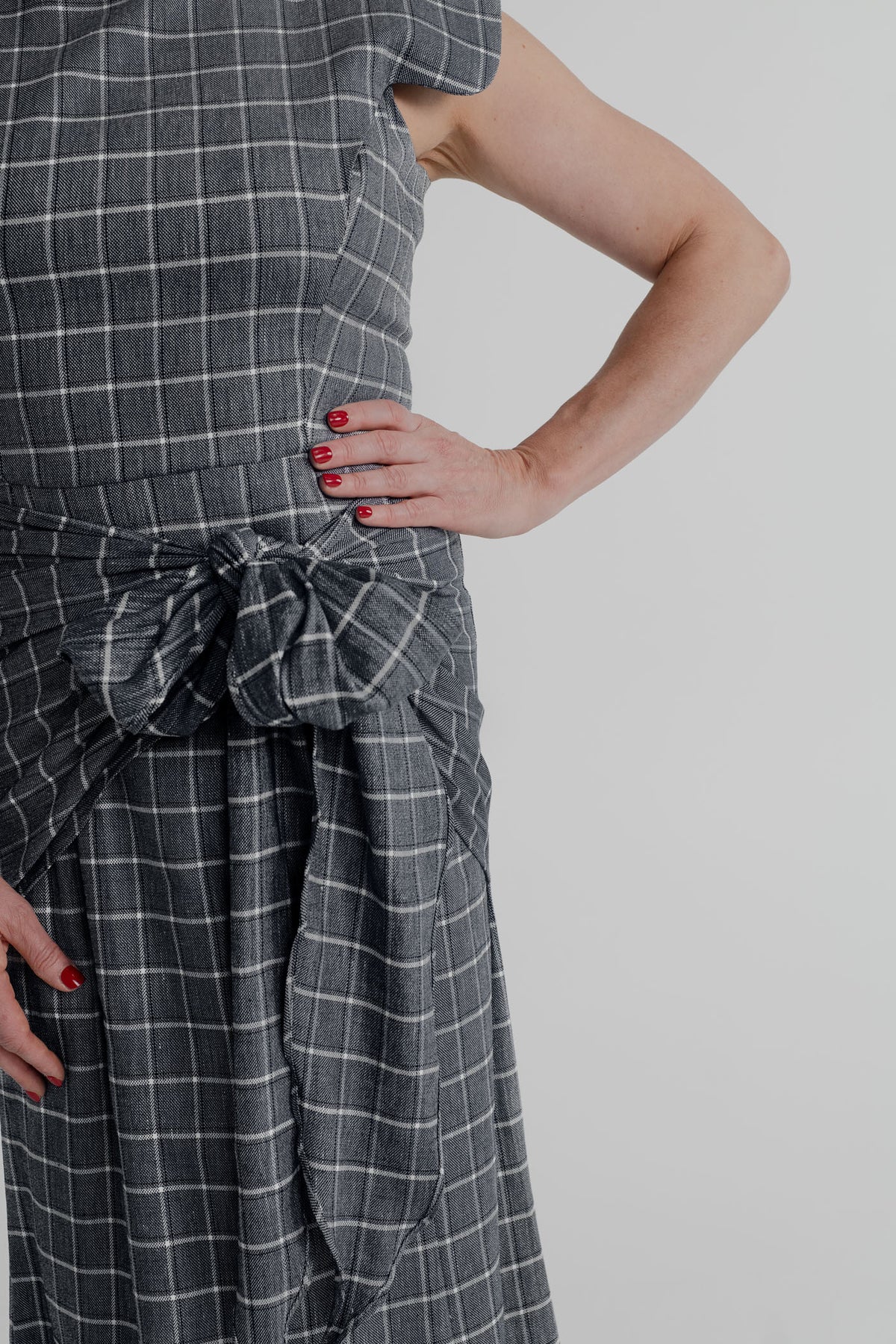Close-up of the IQ Collection Antonia Plaid Maxi showing the charcoal plaid fabric and oversized knotted waist tie detail.
