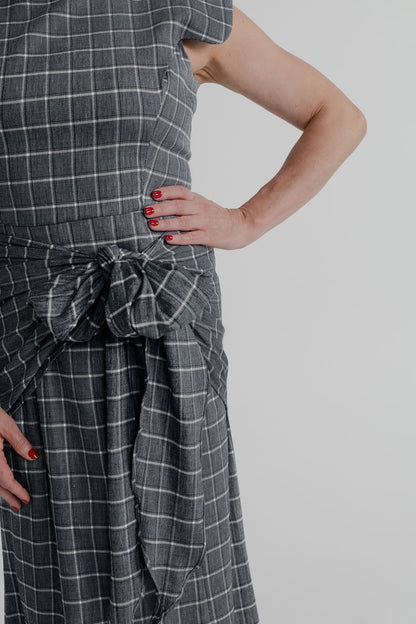 Close-up of the IQ Collection Antonia Plaid Maxi showing the charcoal plaid fabric and oversized knotted waist tie detail.
