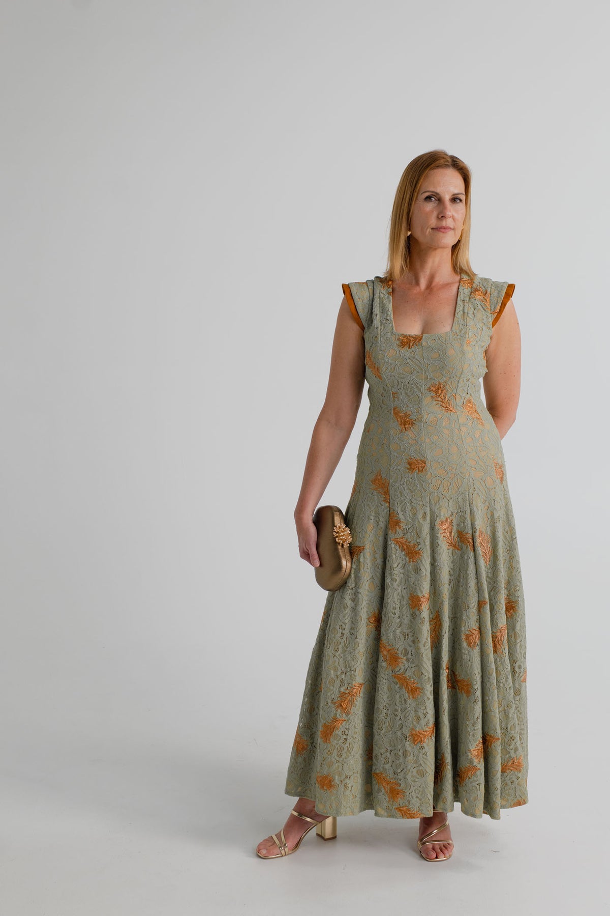 IQ Collection Rose Maxi in sage lace with copper floral embroidery, styled with the Verano Hill Coraline Sculpted clutch and gold heels.
