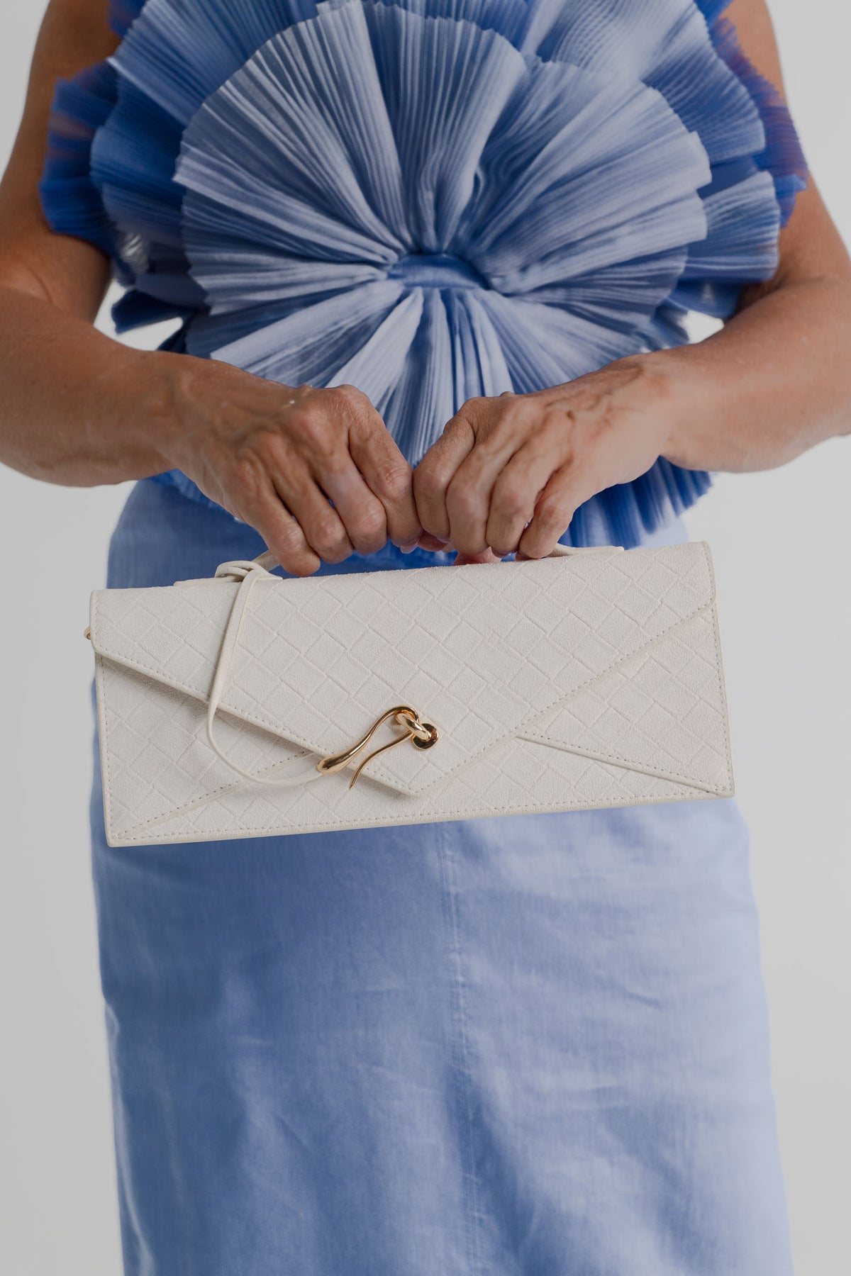 JW Pei Celeste cream woven top handle bag with gold-tone hardware, styled with the sculptural pleated bodice of the Aje Kira blue midi dress.
