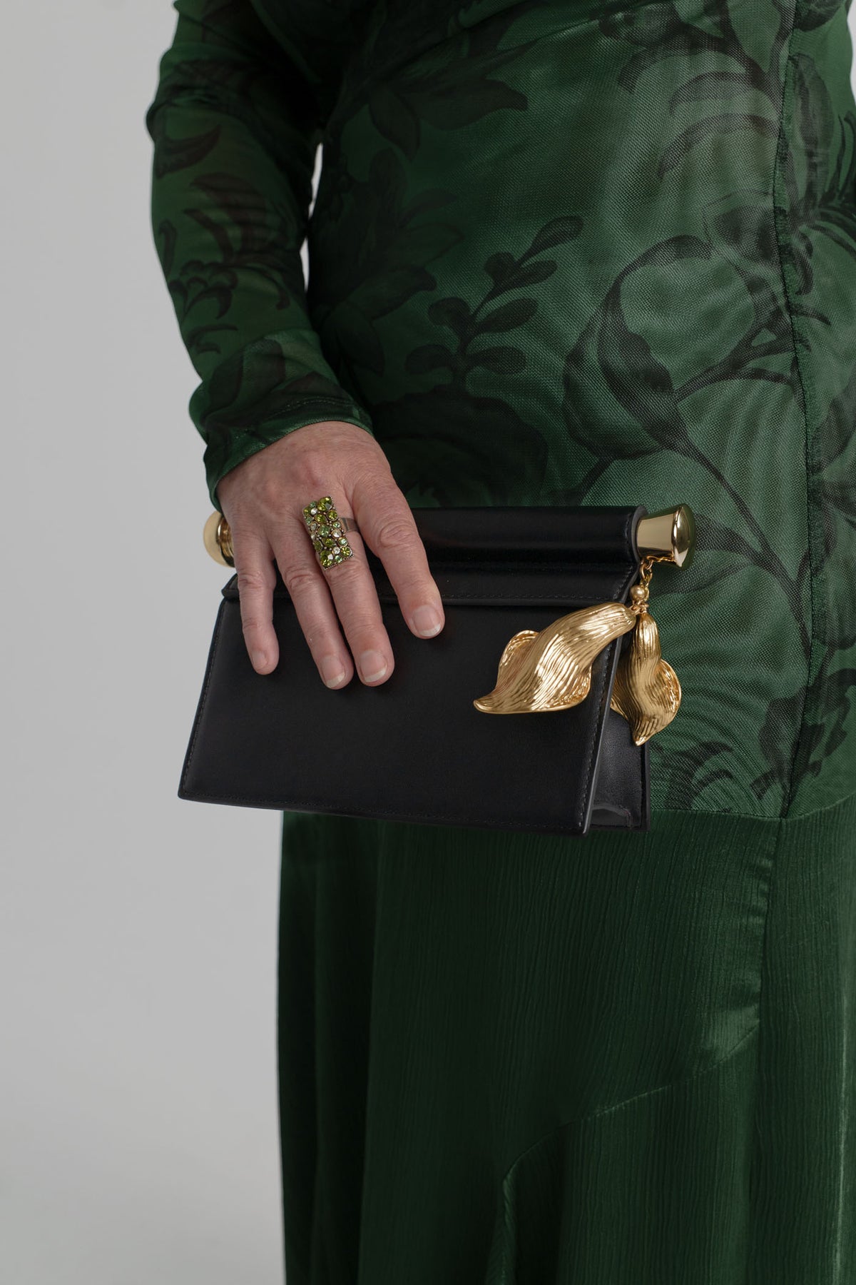 JW Pei Holly black embellished clutch with sculptural gold-tone leaf pendant and bar detail, styled with the One Fell Swoop New Order green floral gown.
