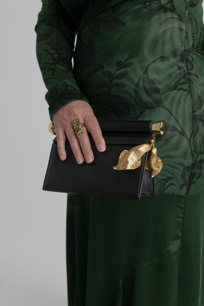 JW Pei Holly black embellished clutch with sculptural gold-tone leaf pendant and bar detail, styled with the One Fell Swoop New Order green floral gown.
