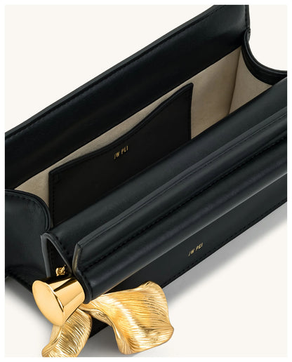 Open view of JW Pei Holly black clutch showing the light interior and gold-tone leaf pendant detail. 
