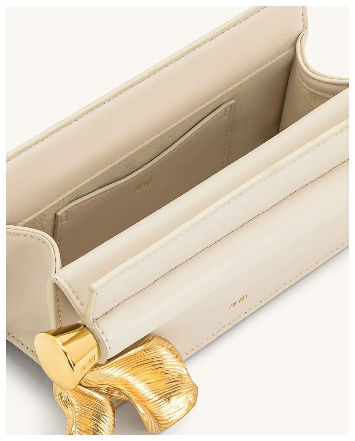 Open view of JW Pei Holly cream clutch showing the light interior and gold-tone leaf pendant detail. 
