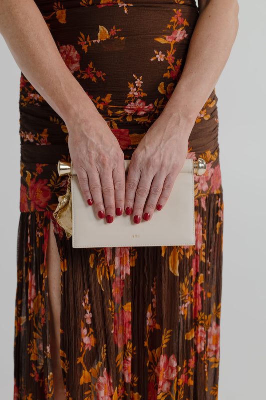Close-up of the JW Pei Holly cream clutch with sculptural gold-tone leaf pendant and bar detail, styled with the Pasduchas Wren chocolate floral maxi dress.
