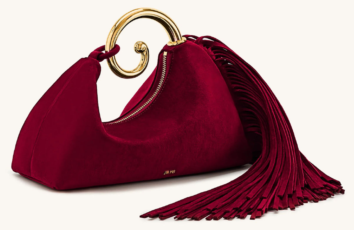 Angled side view of JW Pei Nell burgundy suede fringe bag showing the curved silhouette, zip closure and long fringe detailing. 
