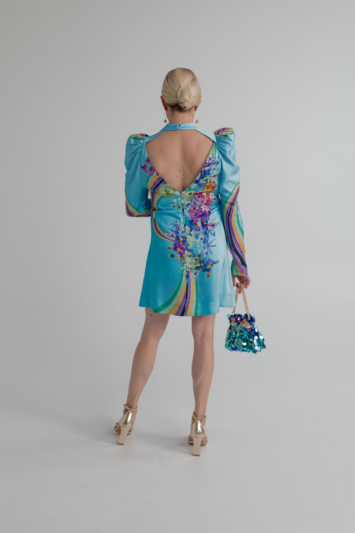Back view of the Mackenzie Mode Hollywood Blooming Mini Dress showing the turquoise satin fabric, puff sleeves, multicolour floral-and-stripe print and open-back detail. 
