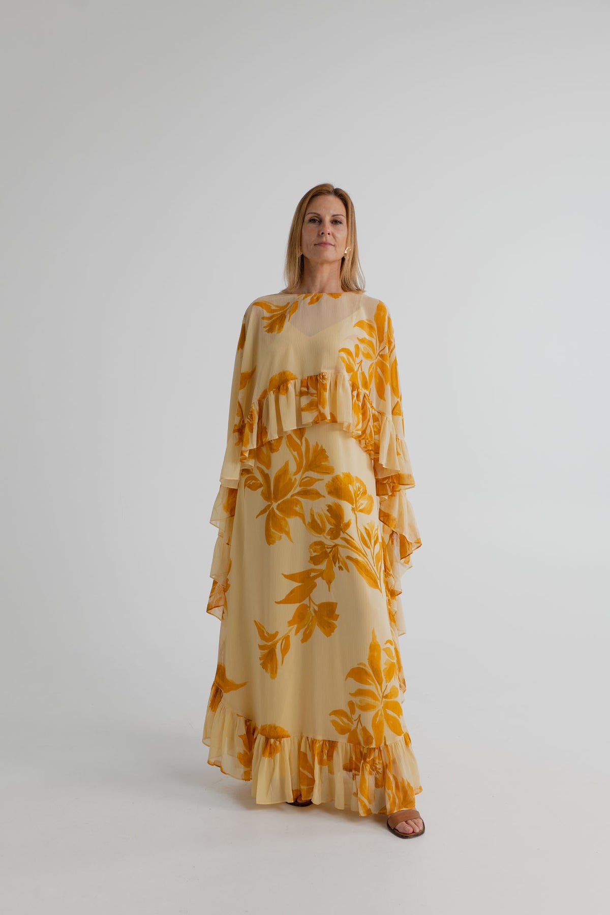 Monsoon Joanna Ruffle Cape Maxi dress in cream with mustard yellow floral print, shown full length from the front with flowing ruffle cape overlay.
