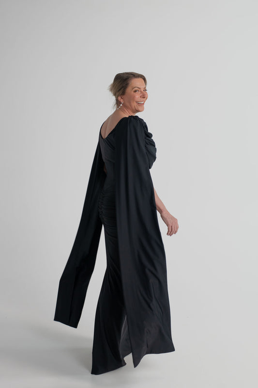 Side and back view of the Mossman Reign black midi dress showing the elongated cape sleeves, open back and fitted silhouette.
