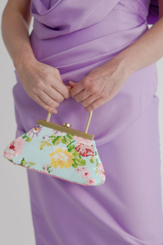 Close-up of the Olga Berg Audrey floral sequin top handle bag with multicolour flower design and gold-tone frame, styled with the Eliya the Label Scarlett lilac dress.
