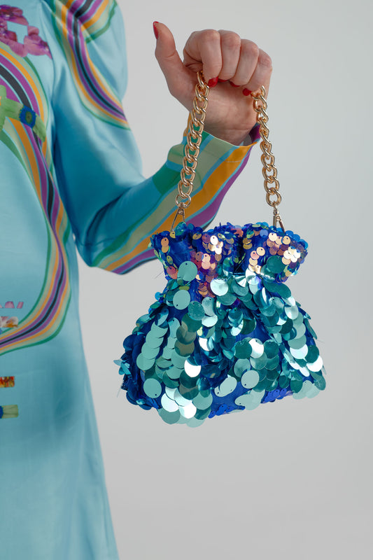 Close-up of the Olga Berg Pedro Sequin Pouch with oversized blue, teal and iridescent sequins, gold chain handle and the turquoise Mackenzie Mode Hollywood Blooming Mini Dress. 
