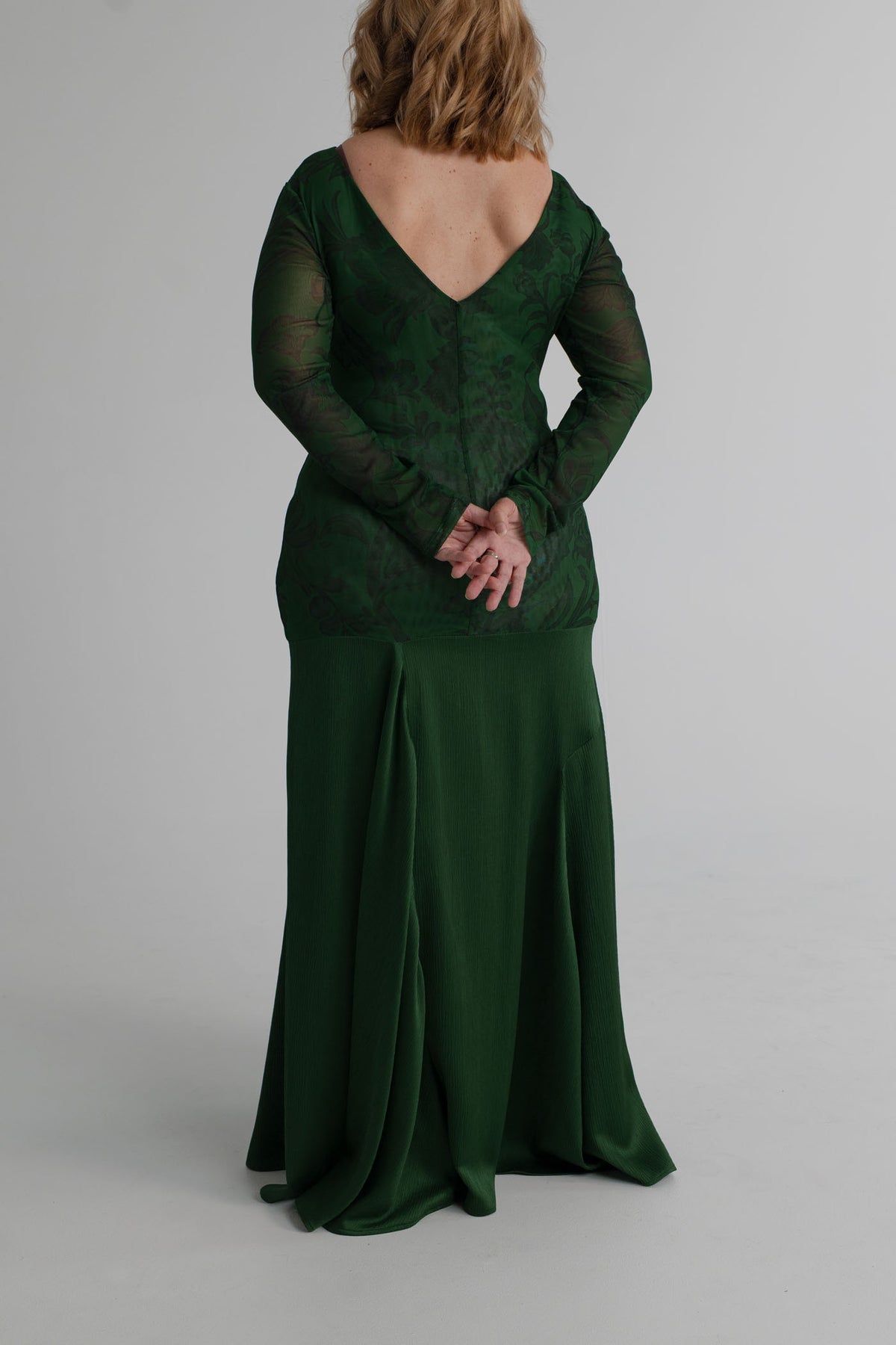 Back view of the One Fell Swoop New Order deep green floral gown showing the V-back, fitted sheer sleeves and flowing full-length skirt.
