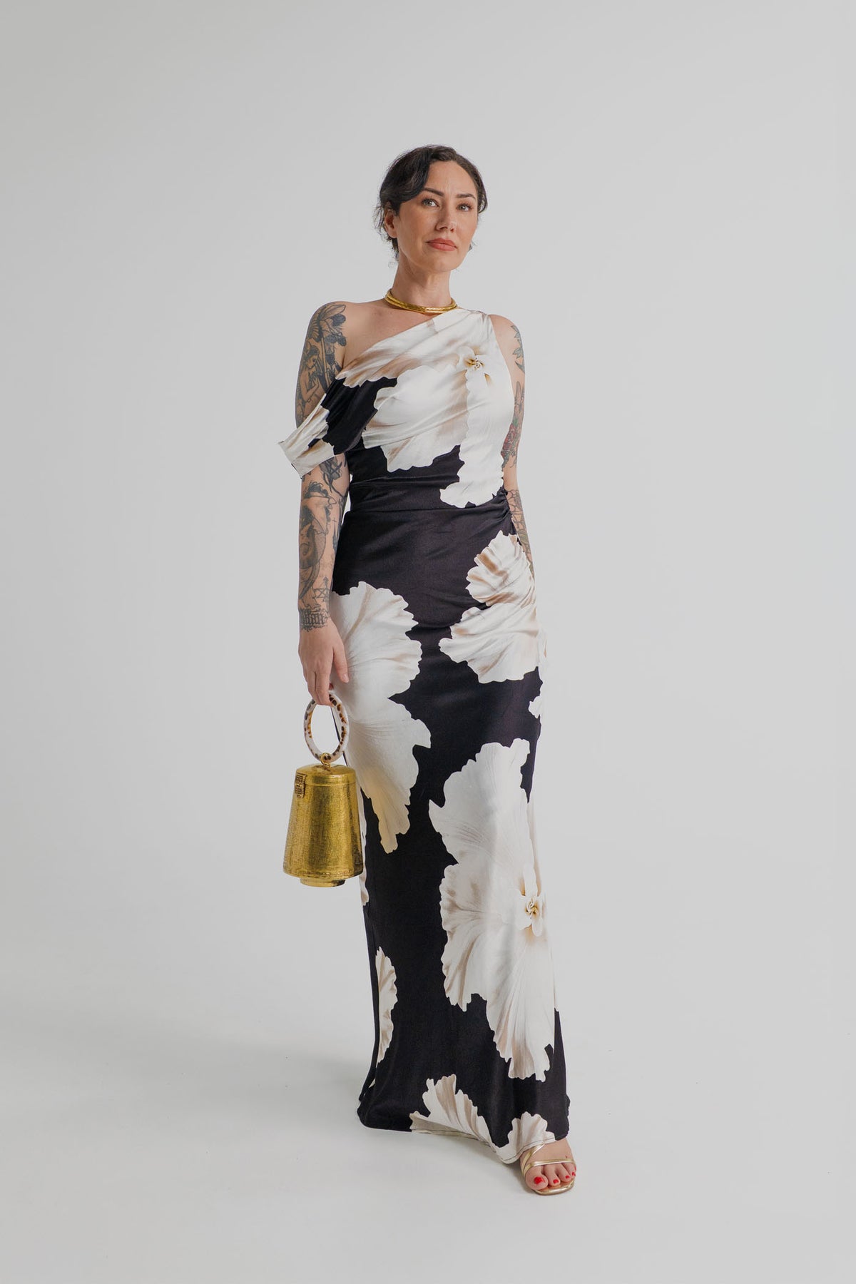 Pasduchas Finley Midnight Bloom black and ivory floral one-shoulder maxi dress styled with The Hold Perception of Time gold top handle bag.
