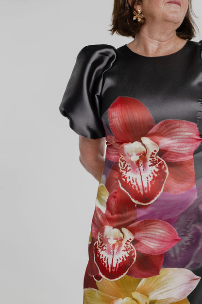 Close-up of the Pasduchas Nova Black Orchid dress showing the oversized red orchid placement print and sculptural black puff sleeve.
