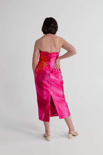 Back view of the Pasduchas Thea Camellia Pink strapless midi dress showing the fitted bodice, centre-back zip and back split.
