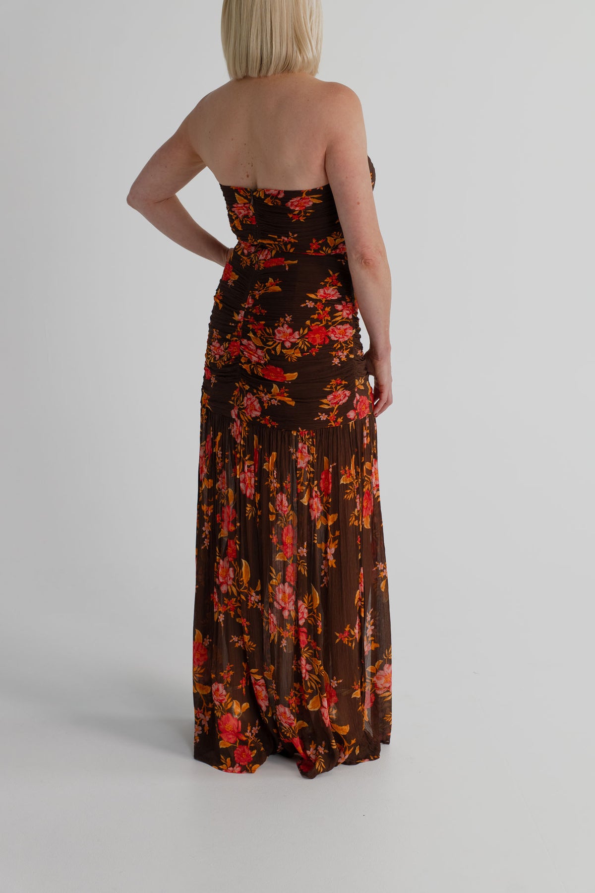 Back view of the Pasduchas Wren chocolate floral strapless maxi dress showing the gathered fitted bodice and flowing full-length skirt.
