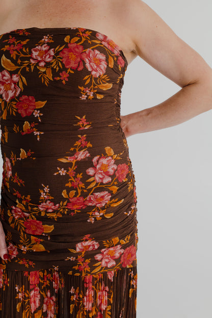 Close-up of the Pasduchas Wren chocolate floral maxi dress showing the strapless neckline, gathered bodice and warm pink, coral and golden floral print.
