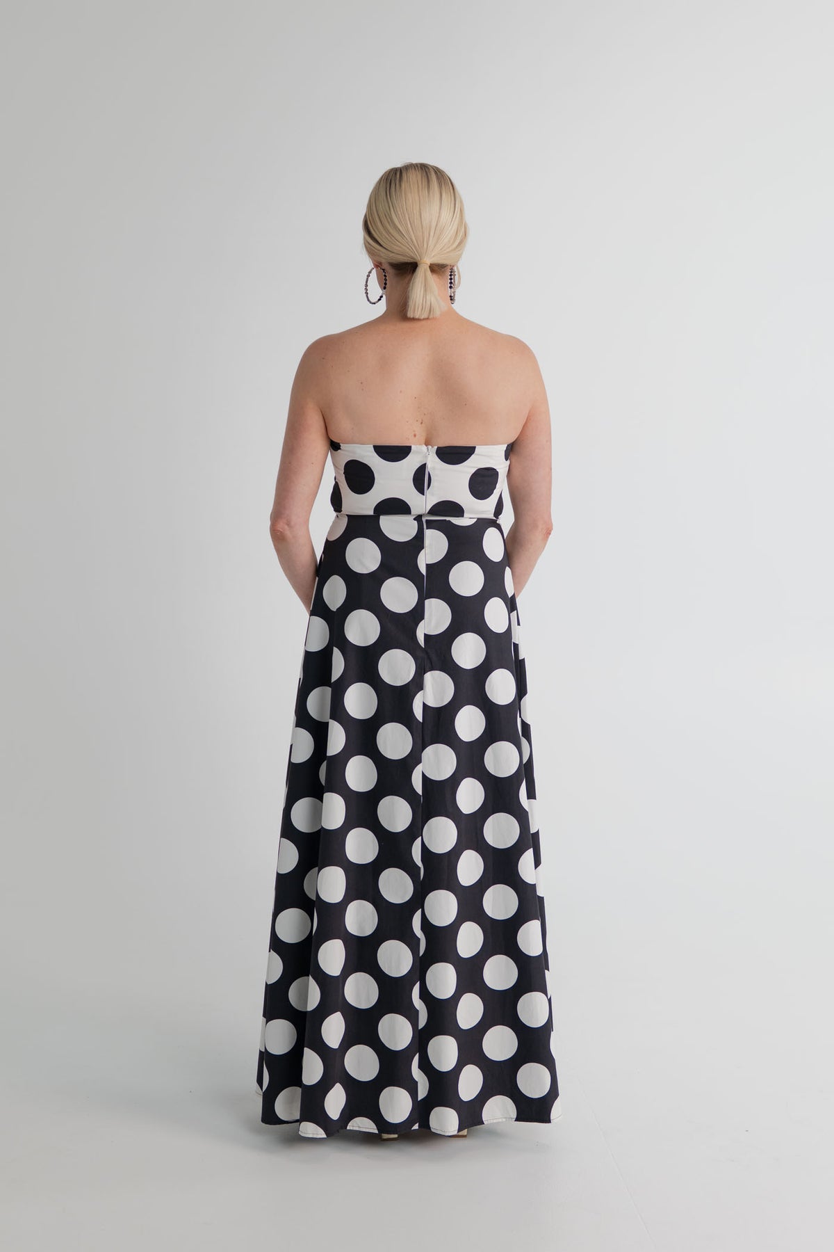 Back view of the Sonya Moda Milano Gown with strapless bodice, fitted waist and full-length black skirt with oversized white polka dots. 
