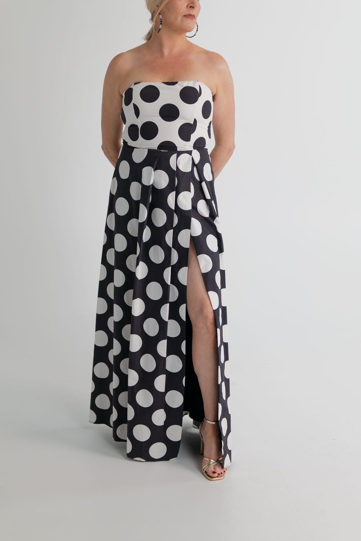 Three-quarter view of the Sonya Moda Milano Gown highlighting the strapless bodice, defined waist, oversized polka dot print and front leg split. 
