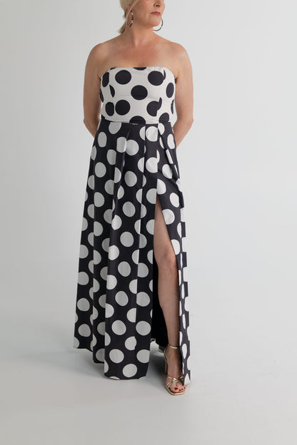 Three-quarter view of the Sonya Moda Milano Gown highlighting the strapless bodice, defined waist, oversized polka dot print and front leg split. 
