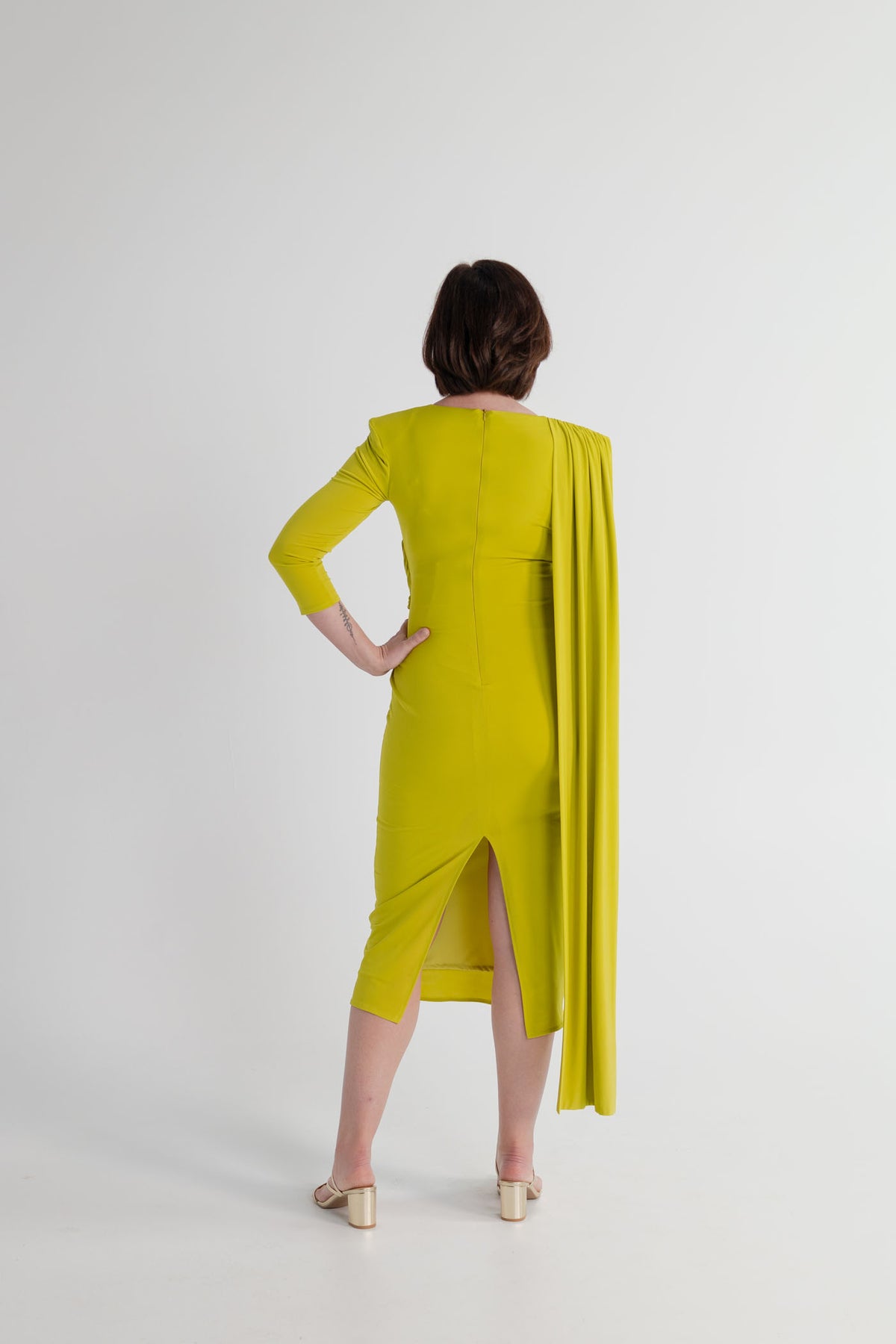 Back view of the chartreuse Strena Barbara Midi Dress showing the fitted midi silhouette, centre back split and long draped shoulder panel.
