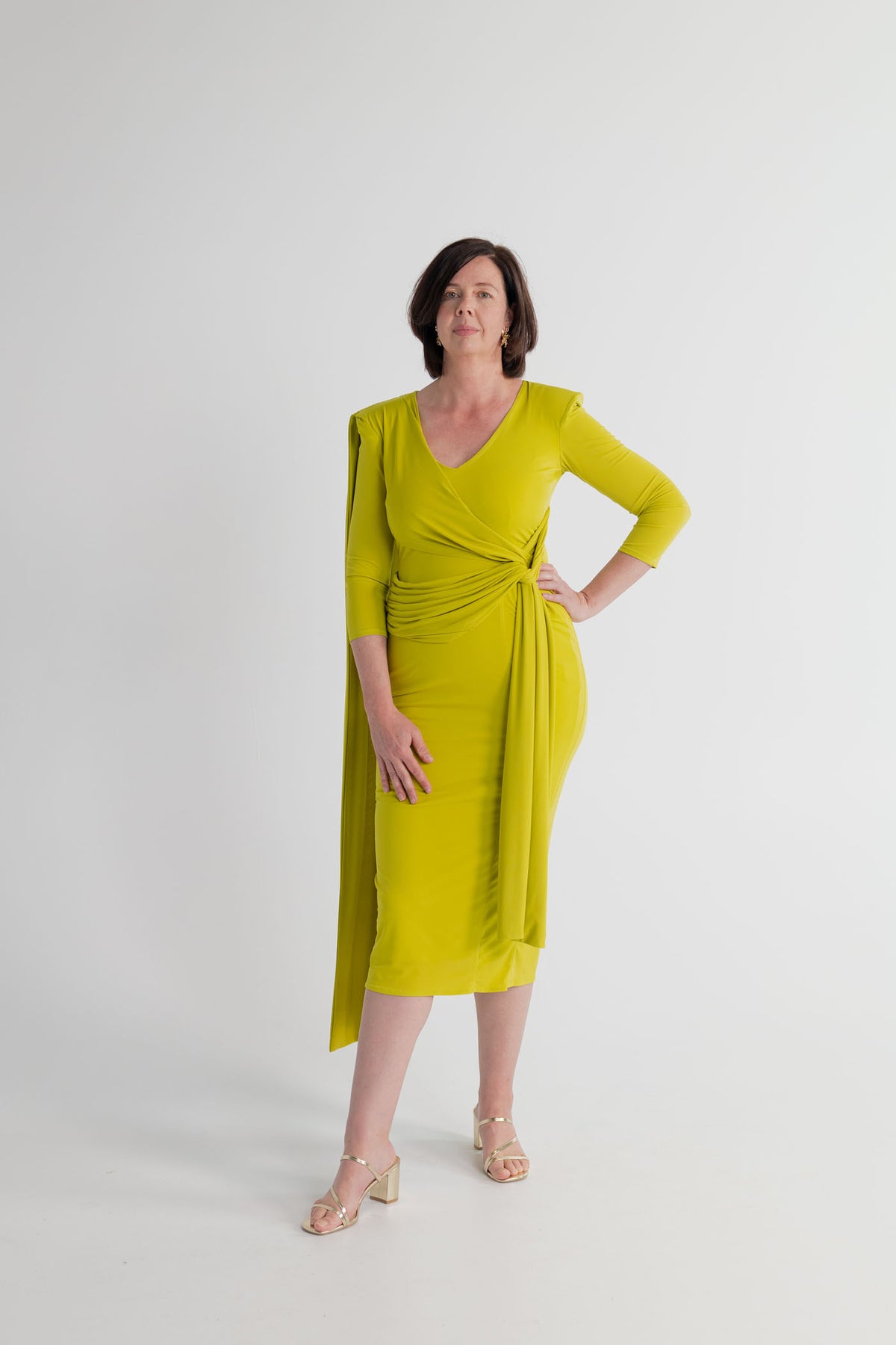 Strena Barbara Midi Dress in chartreuse, shown full length from the front with a V neckline, ruched wrap waist and asymmetric draped shoulder detail.
