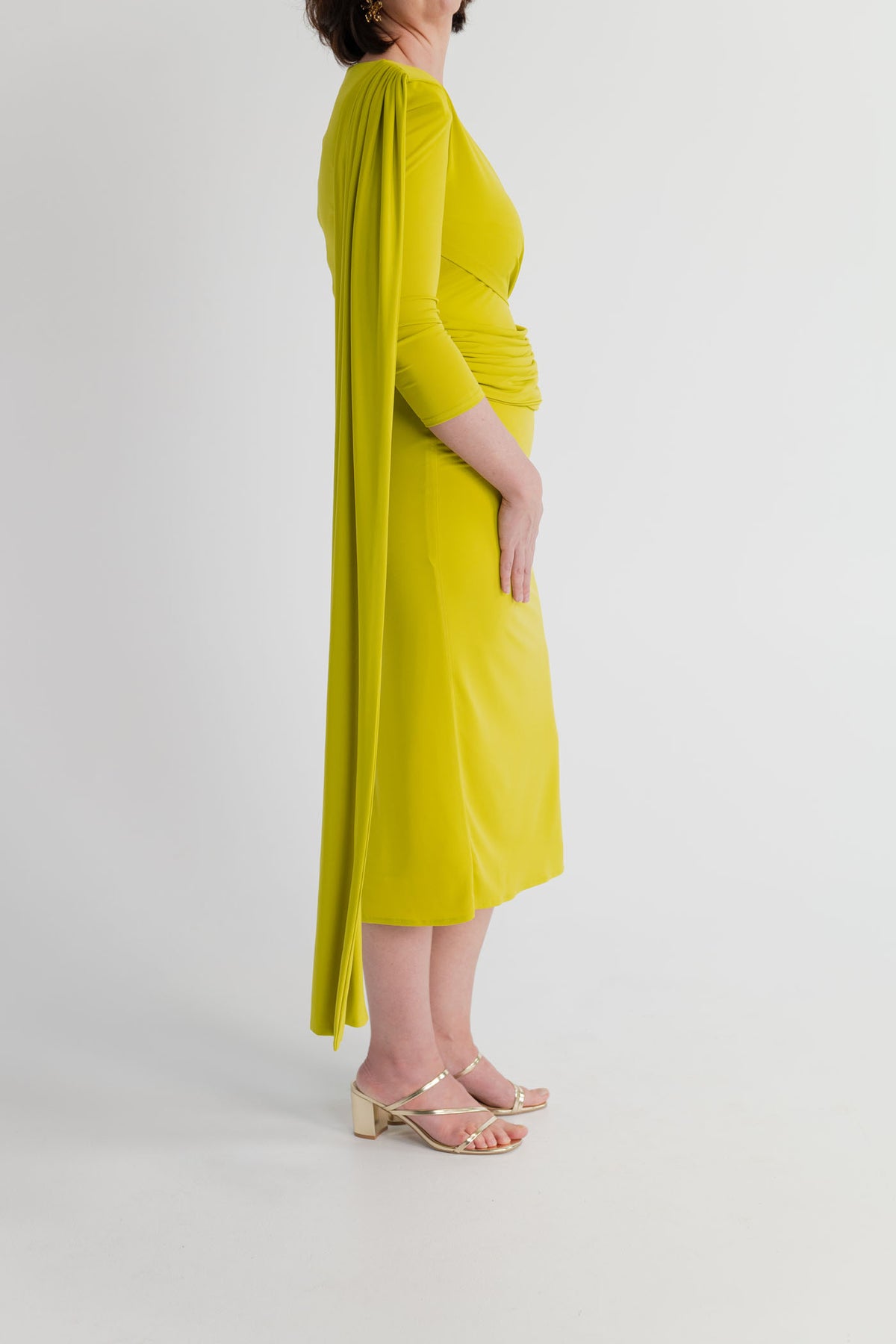 Side view of the chartreuse Strena Barbara Midi Dress highlighting the long asymmetric shoulder drape, fitted waist and midi-length silhouette.

