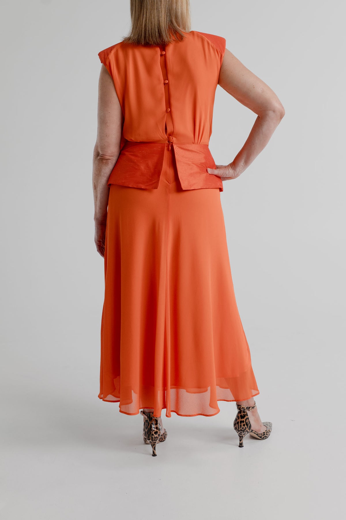 Back view of the orange Strena Diana Midi Dress showing the buttoned bodice, structured waist panel and flowing sheer-overlay midi skirt.
